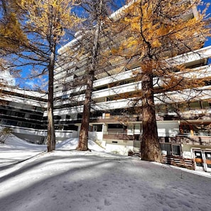 A multi-story building with a modern architectural design, surrounded by trees with autumn foliage and a snowy ground. - Ski-in/ski-out & foot of the slopes, 3rd floor, balcony, tv, 26m², Vars (Vars)
