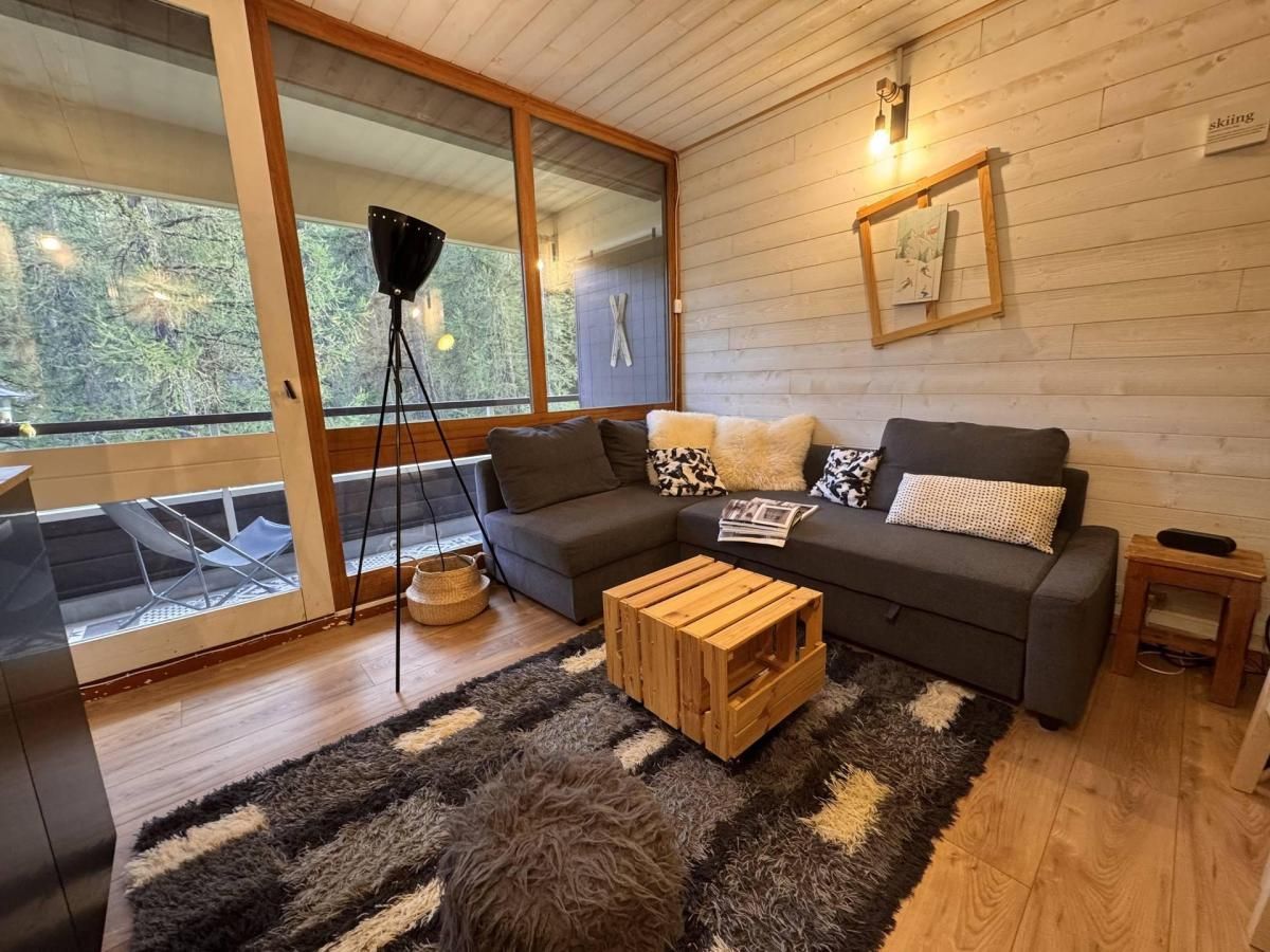A modern living room with a sofa set, a coffee table, and a large window with a view of trees.