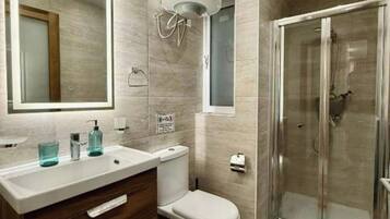 A modern bathroom with a large mirror, a toilet, a shower enclosure, and a vanity with drawers.