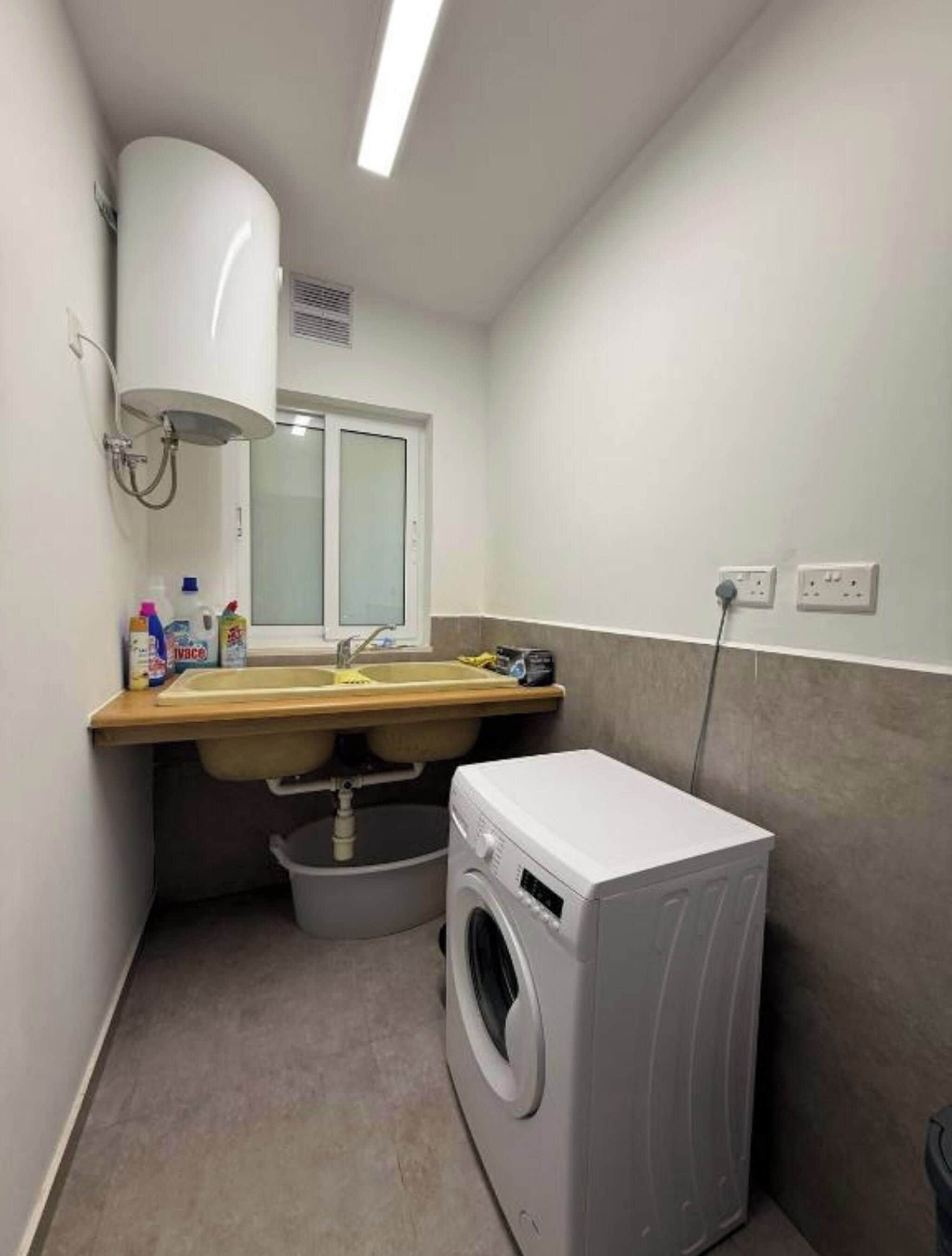 Een wasserette met een wasmachine, een wasbak en een raam.
