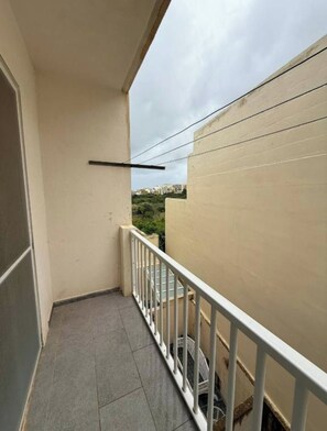 A narrow balcony with a white railing, a tiled floor, and a view of buildings in the distance.