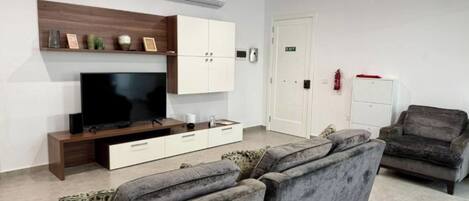 A modern living room with a flat-screen TV, a sofa, a cabinet, and a door marked 'EXIT'.