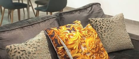 A modern living room with a grey sofa, patterned cushions, and a dining area in the background.