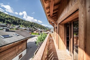 Un balcón de madera con vistas a una zona residencial y una montaña boscosa al fondo.