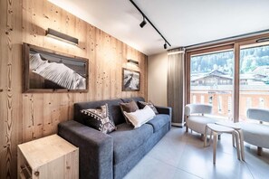 A modern living room with a sofa, a coffee table, and a view of a mountainous landscape through large windows. - 350m from ski lifts, 2nd floor, balcony, parking, tv, ski locker, 41m², Morzine (Morzine)
