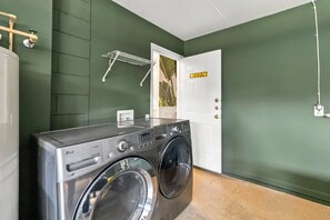 A laundry room with a front-loading washing machine, a drying rack, and a door with a caution sign. - 4/2 Vacation Home at Windsor Palms!! (Kissimmee)