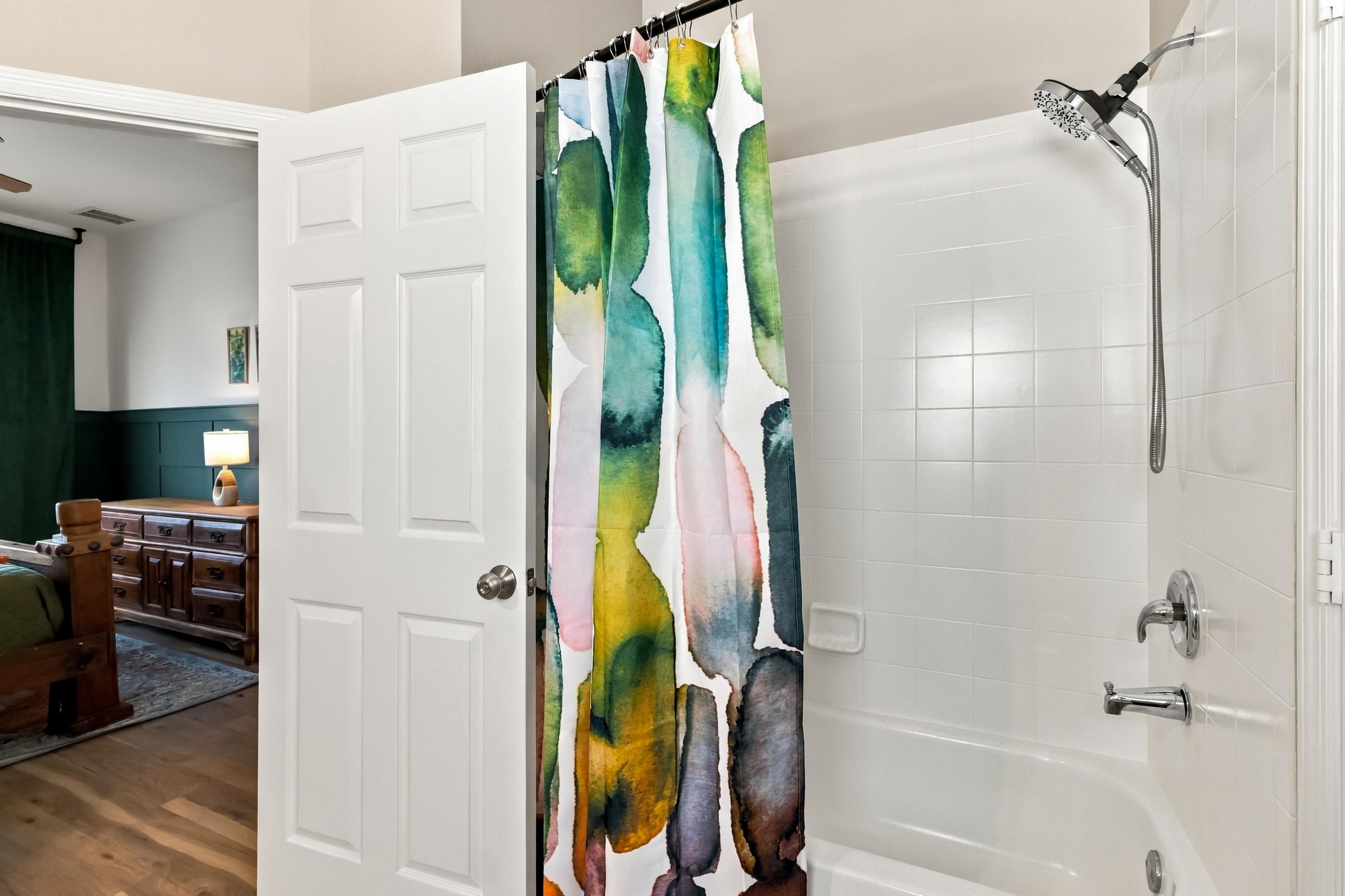 Un baño con ducha, una puerta blanca y una cortina de baño colorida.
