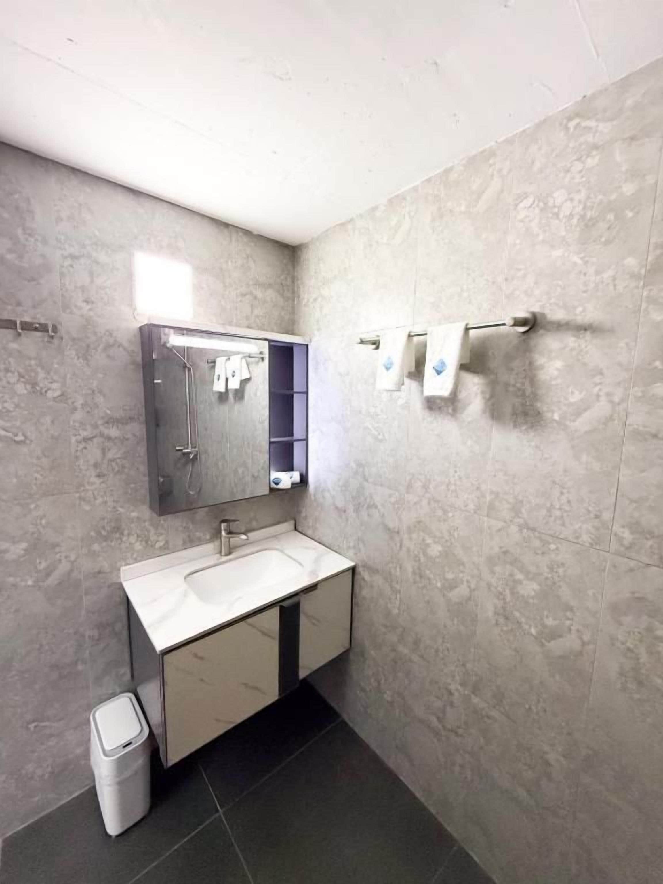 A bathroom with a white sink, a mirror, a towel rack, and a trash bin.