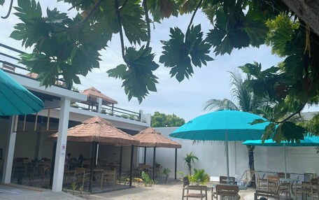 An outdoor seating area with tables and chairs, surrounded by thatched umbrellas and palm trees.