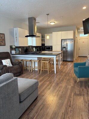 A modern kitchen with white cabinets, a stainless steel refrigerator, and a central island with stools. - Three bedroom house in charming Galveston.  Close to beach and restaurants, (Galveston)