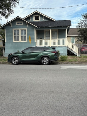 A green SUV parked in front of a two-story house with a porch and a staircase leading to the second floor. - Three bedroom house in charming Galveston.  Close to beach and restaurants, (Galveston)