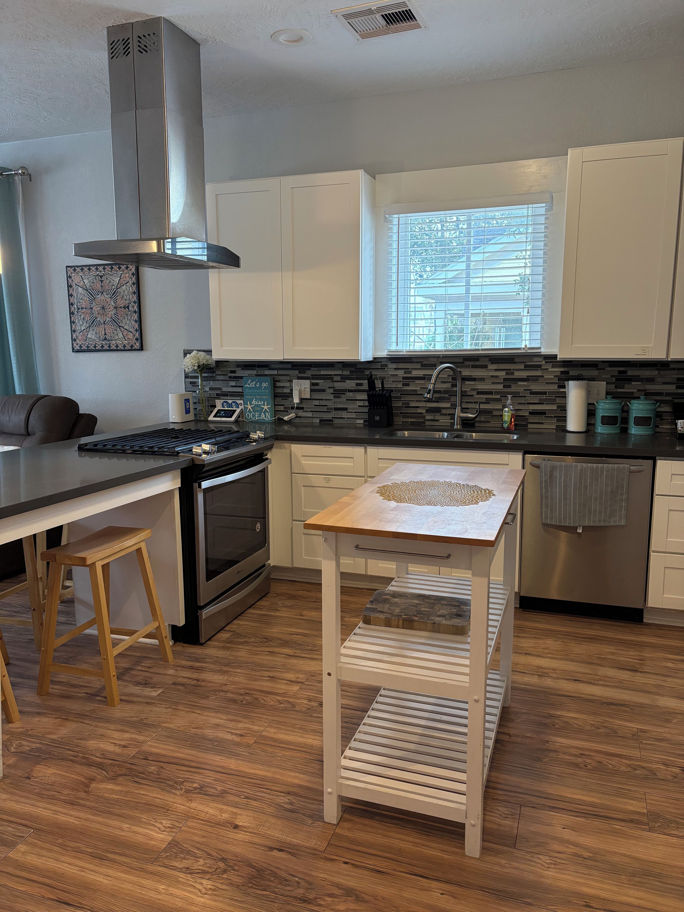 A modern kitchen with a central island, stainless steel appliances, and a window with blinds.