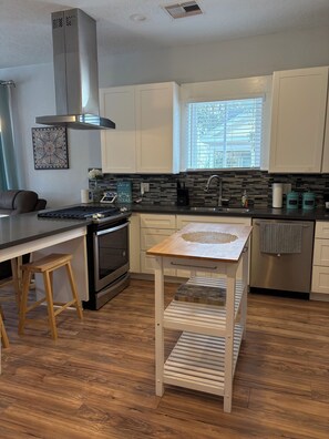 A modern kitchen with a central island, stainless steel appliances, and a window with blinds. - Three bedroom house in charming Galveston.  Close to beach and restaurants, (Galveston)