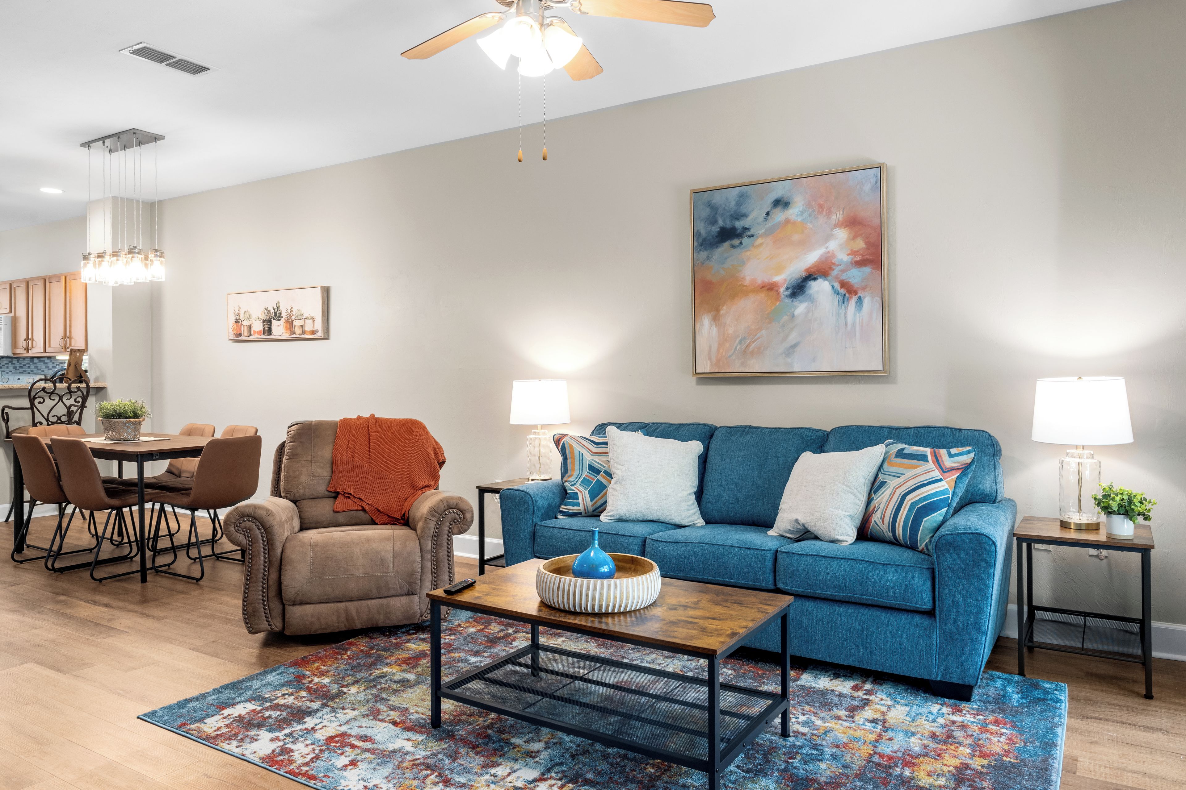 A modern living room with a blue sofa, a brown armchair, a coffee table, and a colorful rug.
