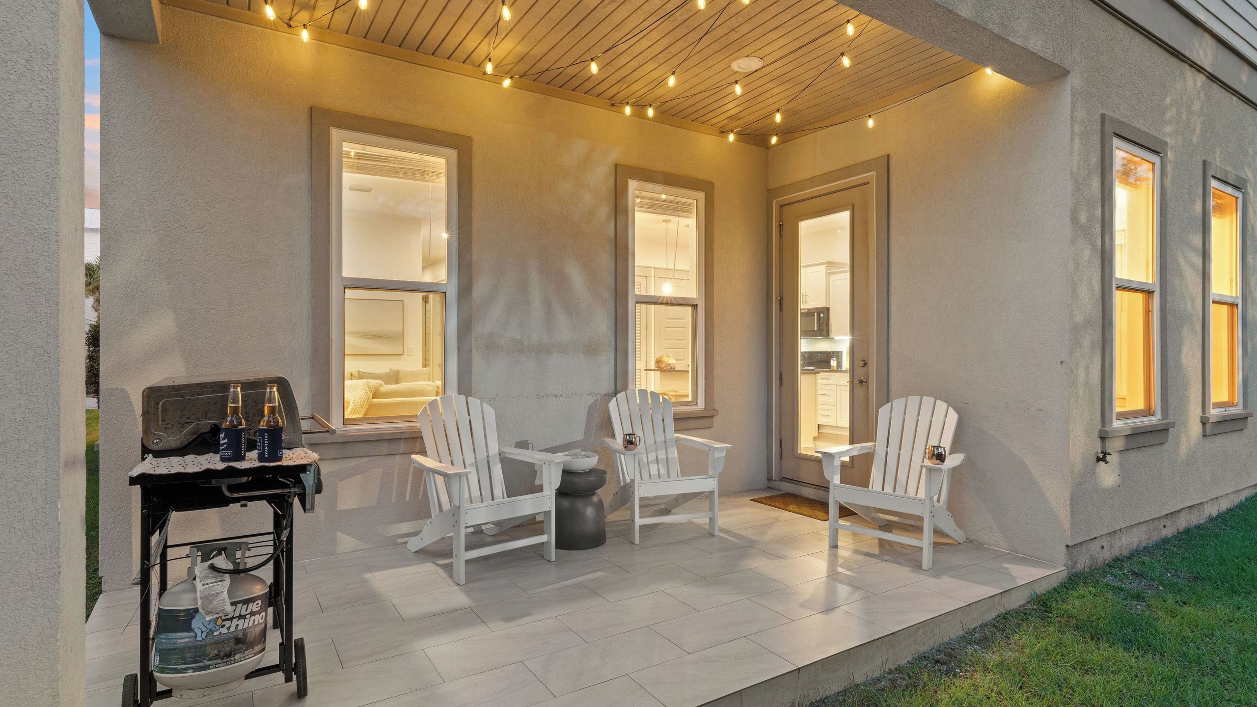 Un patio al aire libre con sillas Adirondack blancas, una mesita y un carrito con botellas.