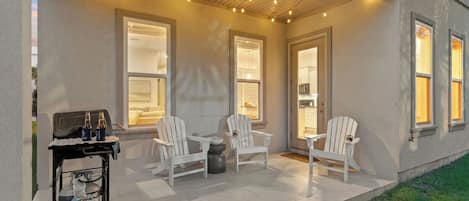 An outdoor patio with white Adirondack chairs, a small table, and a cart with bottles.