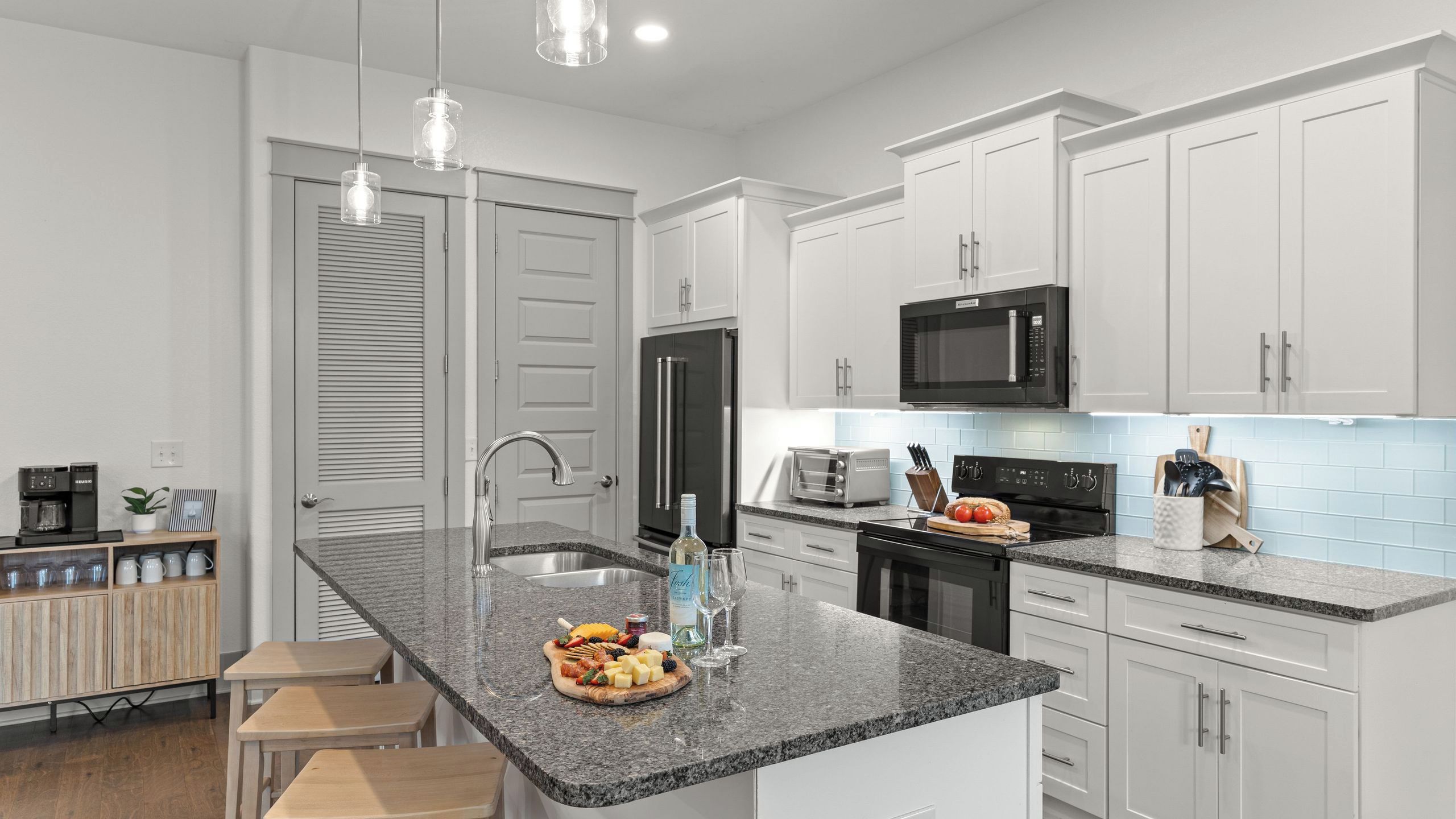Eine moderne Küche mit weißen Schränken, einer Granit-Arbeitsplatte, einem Edelstahl-Kühlschrank, einer Mikrowelle und einem eingebauten Backofen.