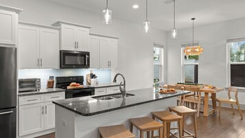 A modern kitchen with white cabinetry, a central island, stainless steel appliances, and a dining area with wooden furniture.