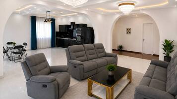A modern living room with grey sofas, a glass dining table, and a black coffee table.