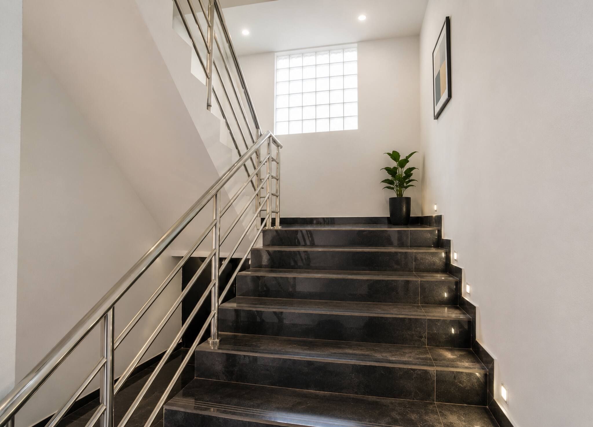 A staircase with a metal railing, leading to a landing with a potted plant.