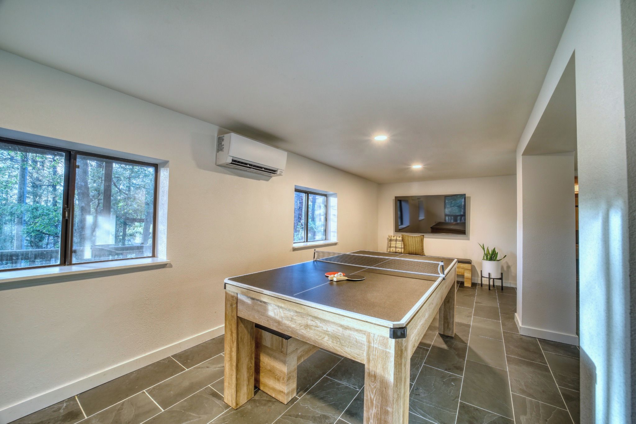 A room with a ping pong table, a small seating area, and large windows.