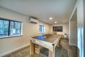 Una habitación con mesa de ping pong, un pequeño rincón de descanso y ventanas amplias.