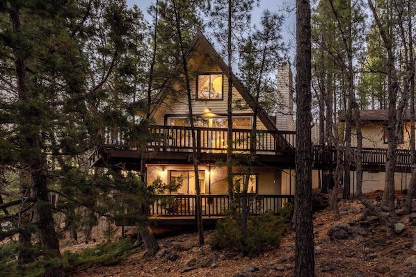 A cabin with a wooden exterior, multiple decks, and a warm interior light.