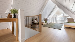 Ein Schlafzimmer im Loft-Stil mit schrägverdeckter Decke, Holzboden, einem Bett, einer Sitzecke und einem kleinen Tisch mit einer Pflanze.
