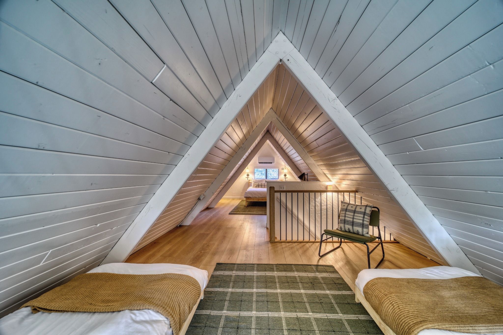 A triangular attic bedroom with a bed, a chair, and a view of the living area.