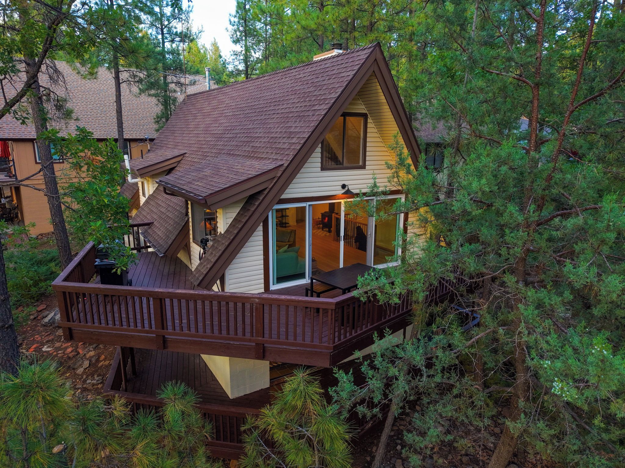A cabin with a deck, large windows, and a chimney.