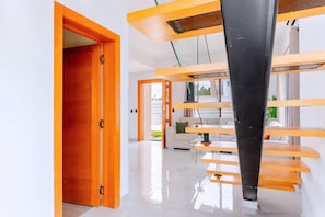 Un intérieur moderne avec un escalier en bois, une porte blanche et une vue sur l’extérieur.