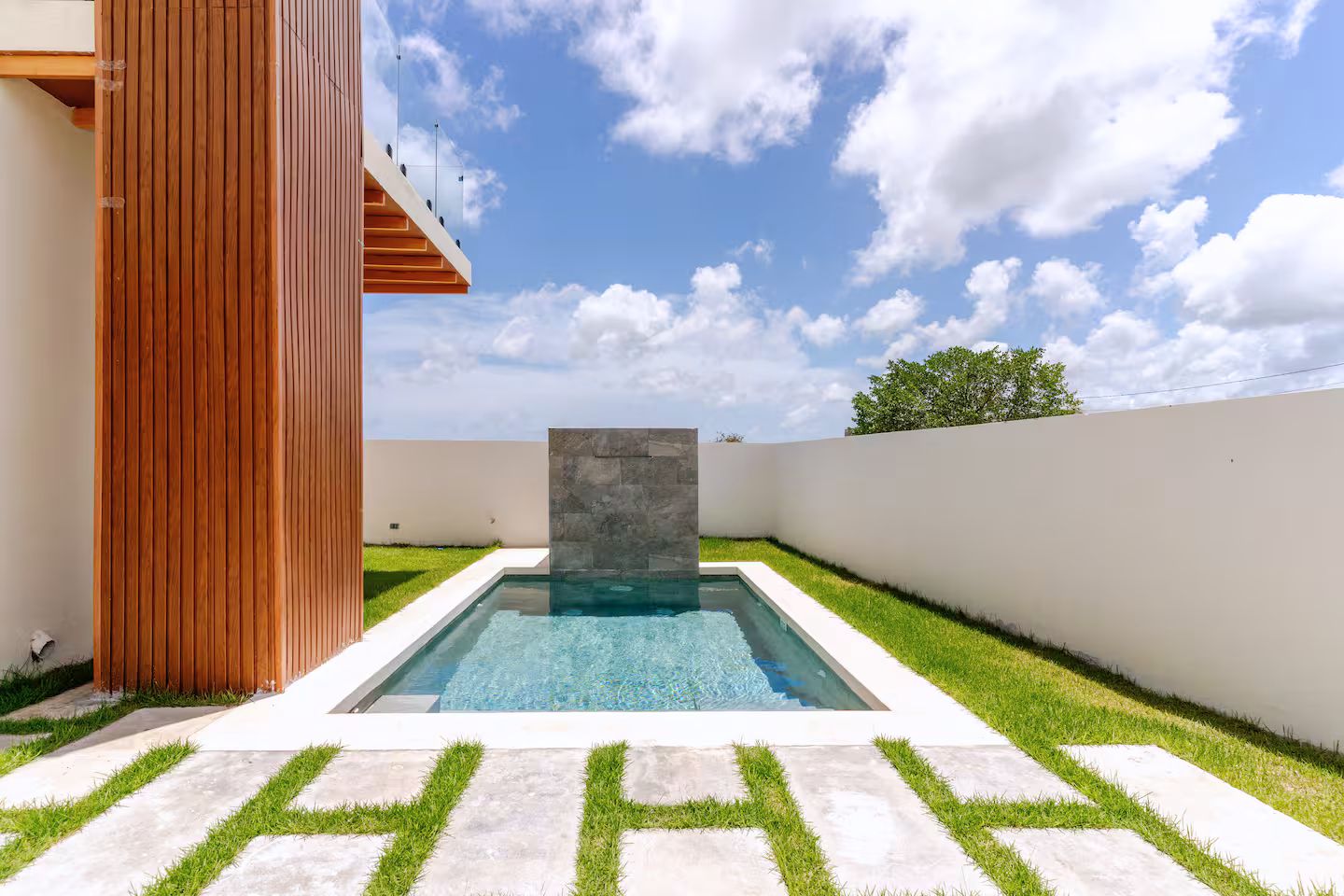 A swimming pool with a stone accent wall, surrounded by a well-maintained lawn and a wooden structure.