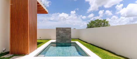 A swimming pool with a stone accent wall, surrounded by a well-maintained lawn and a wooden structure.