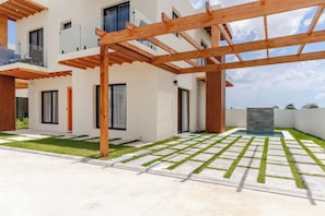En modern bostadsbyggnad med en träpergola, en swimmingpool och en välskött gräsmatta.