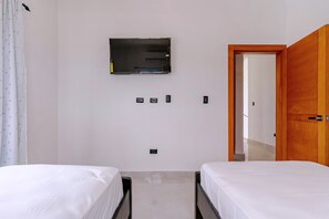 Ein Hotelzimmer mit zwei Betten, einem an der Wand befestigten Flachbildfernseher und einer Holztür, die in einen anderen Raum führt.