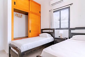Une chambre d’hôtel avec deux lits, une armoire, une table de chevet et une fenêtre.