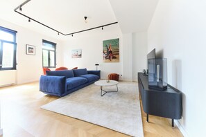 A modern living room with a blue sofa, a white coffee table, and a flat-screen TV on a black stand. - Stylish Apartement in The Heart of the City (Ixelles)