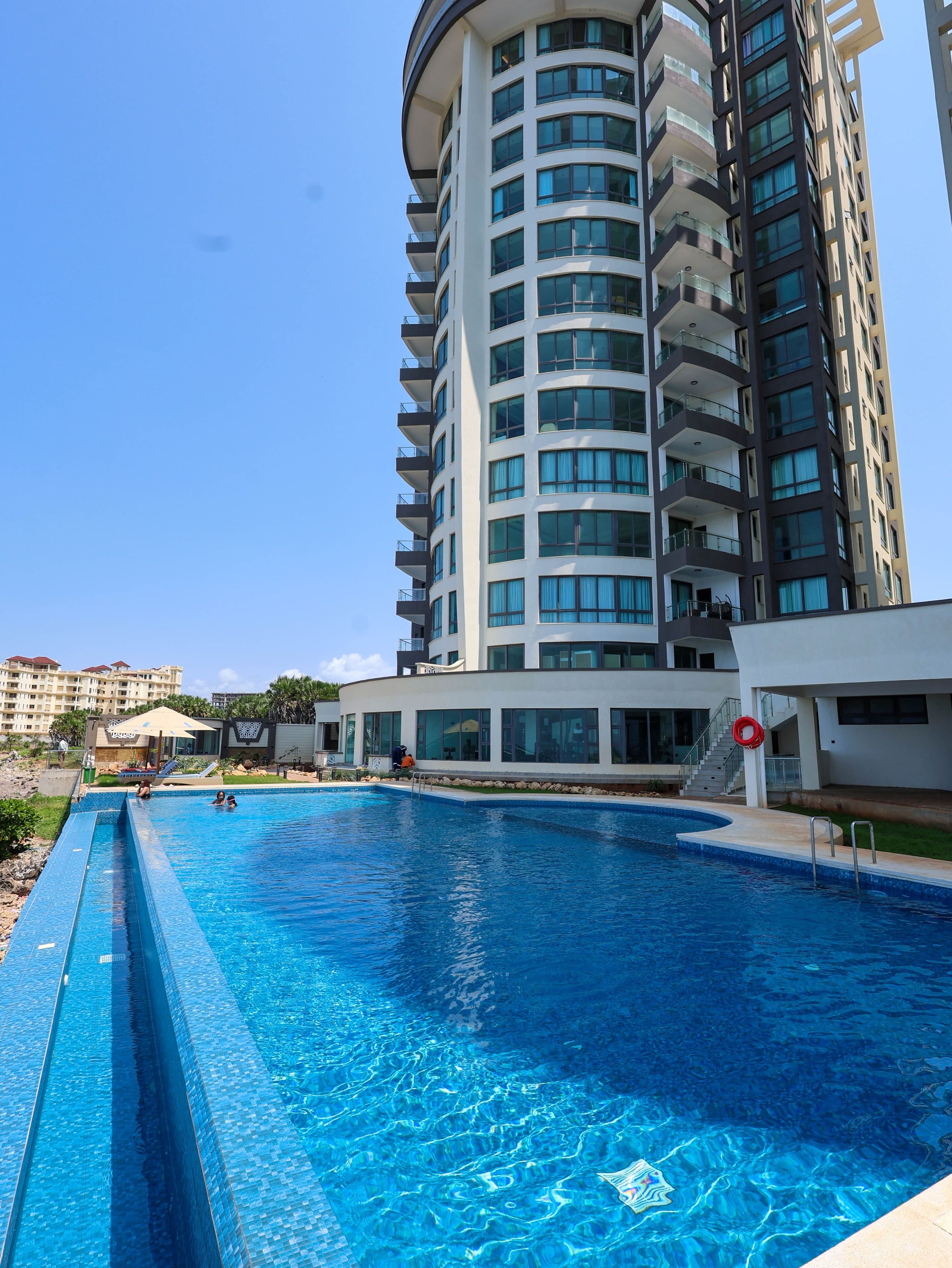 A swimming pool with a clear blue water surface, surrounded by a modern building with multiple balconies and large windows.
