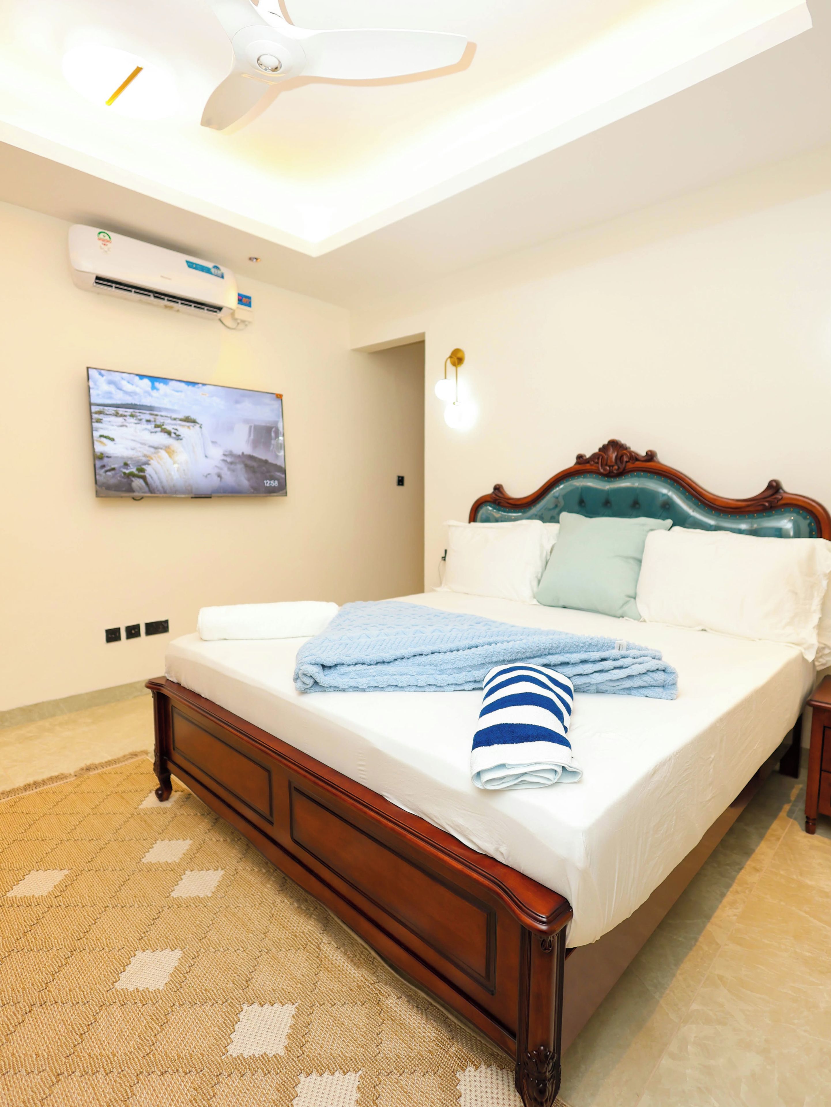 A bedroom with a wooden bed, a flat-screen TV mounted on the wall, and a ceiling fan.