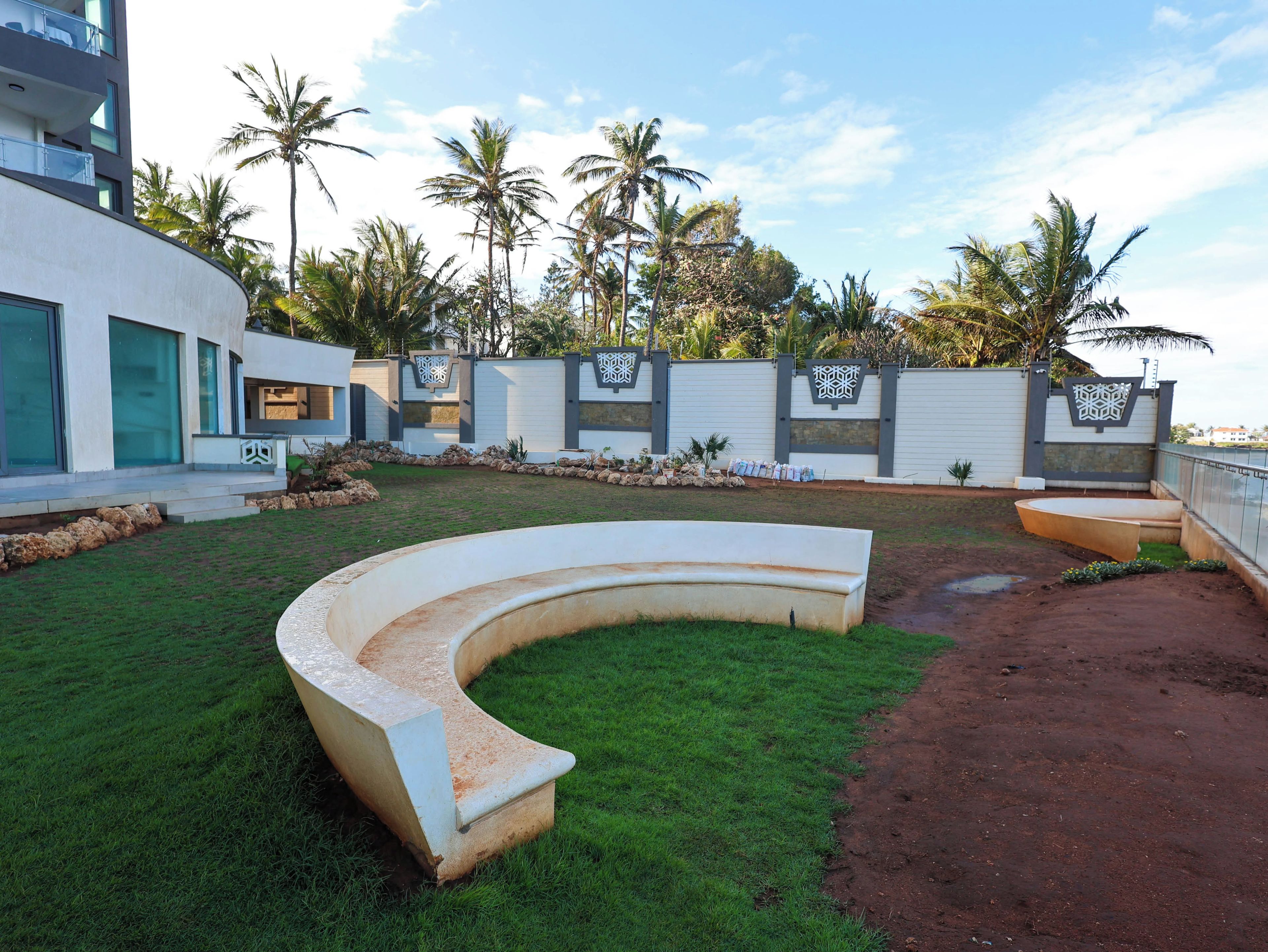 A modern outdoor area with a curved seating area, a paved path, and a white wall with decorative panels.