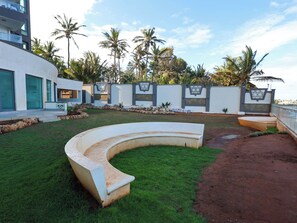 A modern outdoor area with a curved seating area, a paved path, and a white wall with decorative panels.