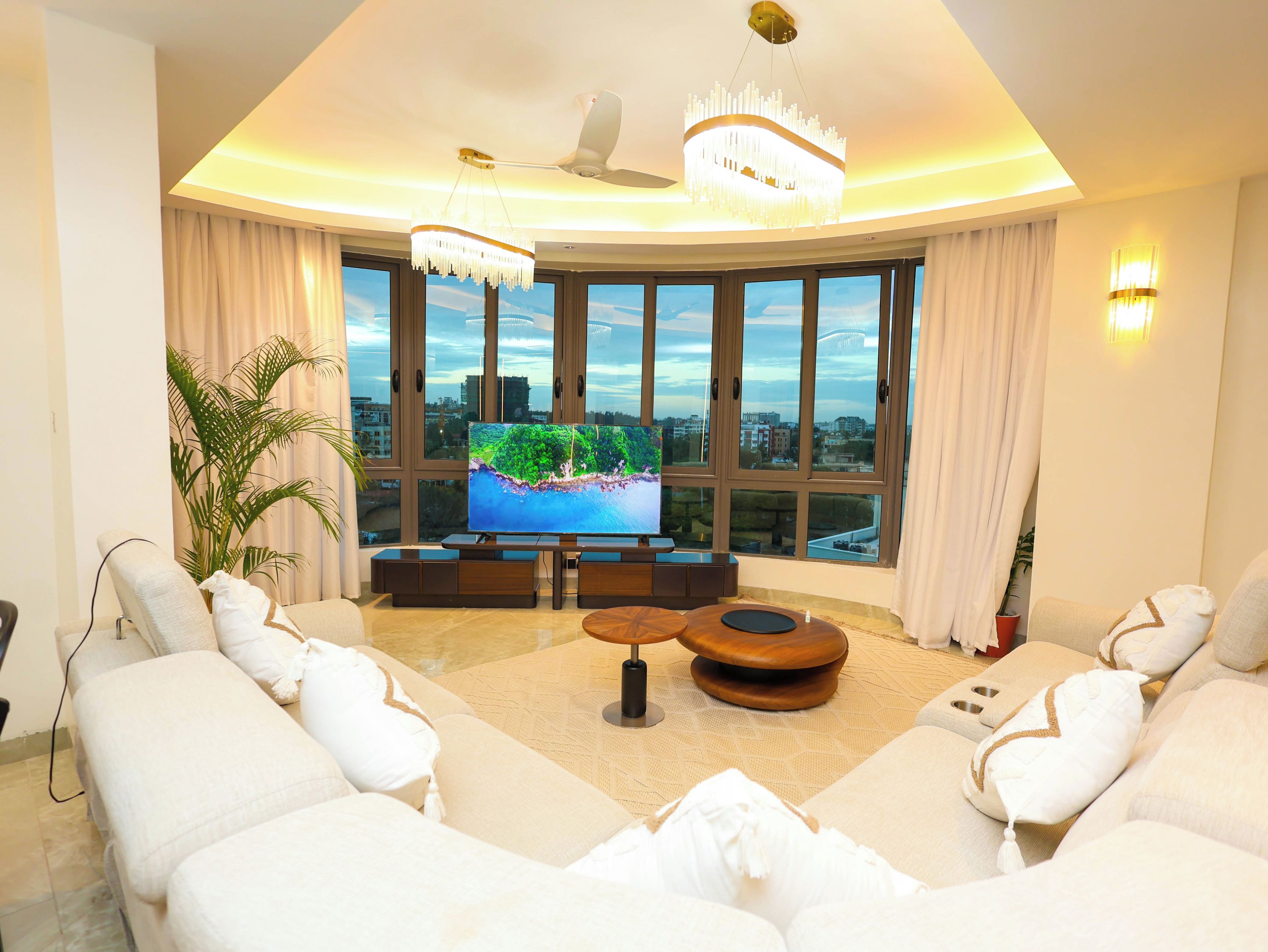 Ein modernes Wohnzimmer mit großem Fernseher, bequemen Sitzmöglichkeiten und Blick auf die Stadt.