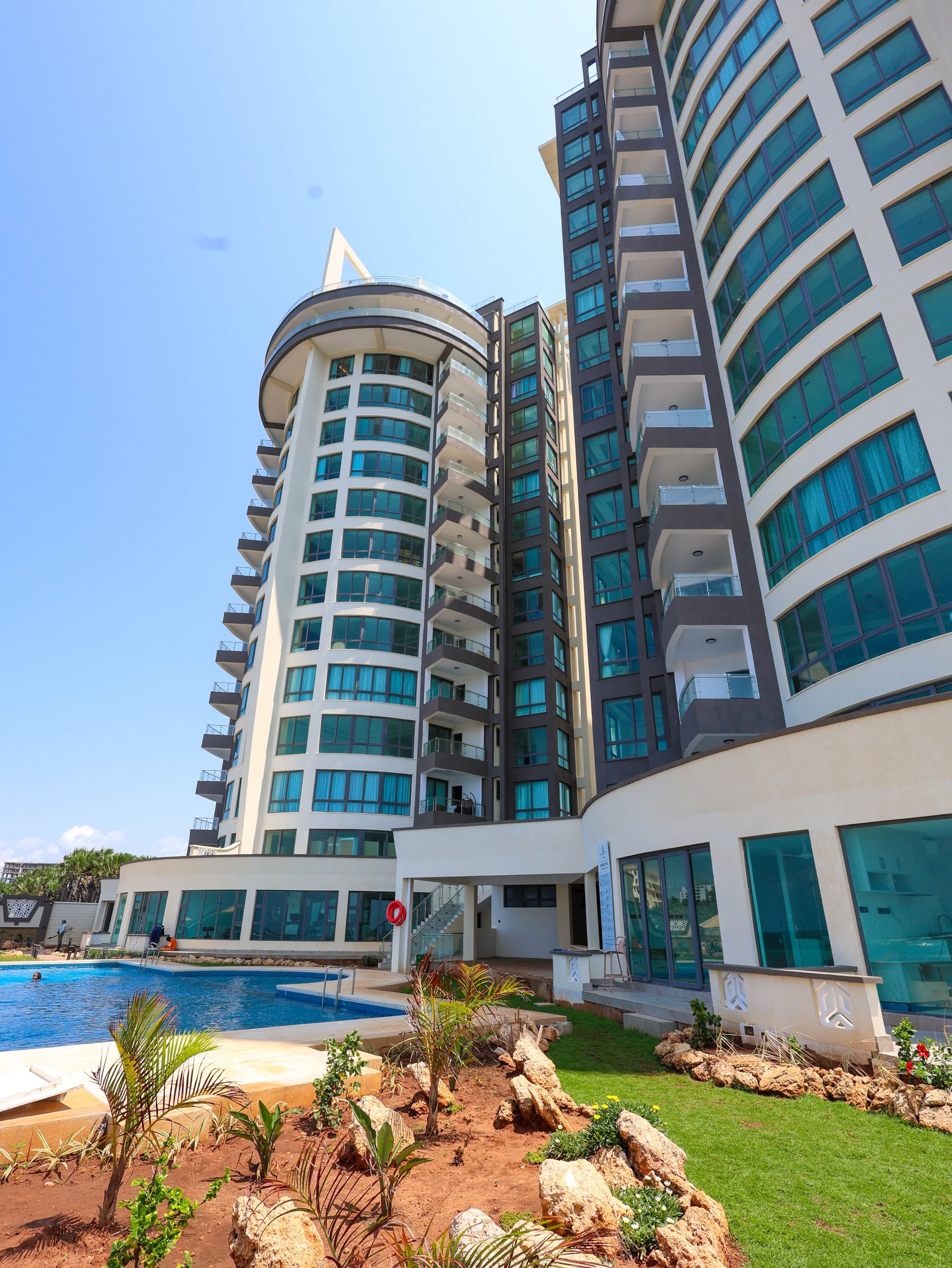 A modern hotel with a pool, multiple balconies, and a curved architectural design.
