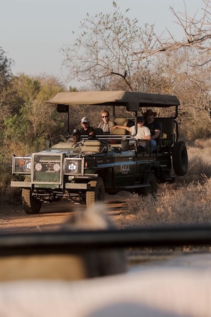 Un véhicule de safari transportant quatre passagers, traversant un paysage aride et couvert de broussailles.