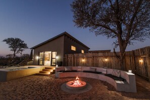 Une maison moderne avec un foyer extérieur dans le jardin, une clôture en bois et un arbre.