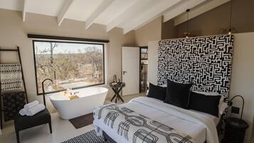 Une chambre moderne avec une grande fenêtre, une baignoire et un lit avec une literie à motifs.