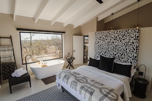 A modern bedroom with a large window, a bathtub, and a bed with patterned bedding. - Beautiful private villa on a Big 5 Reserve with plunge pool, game drives (Hoedspruit)