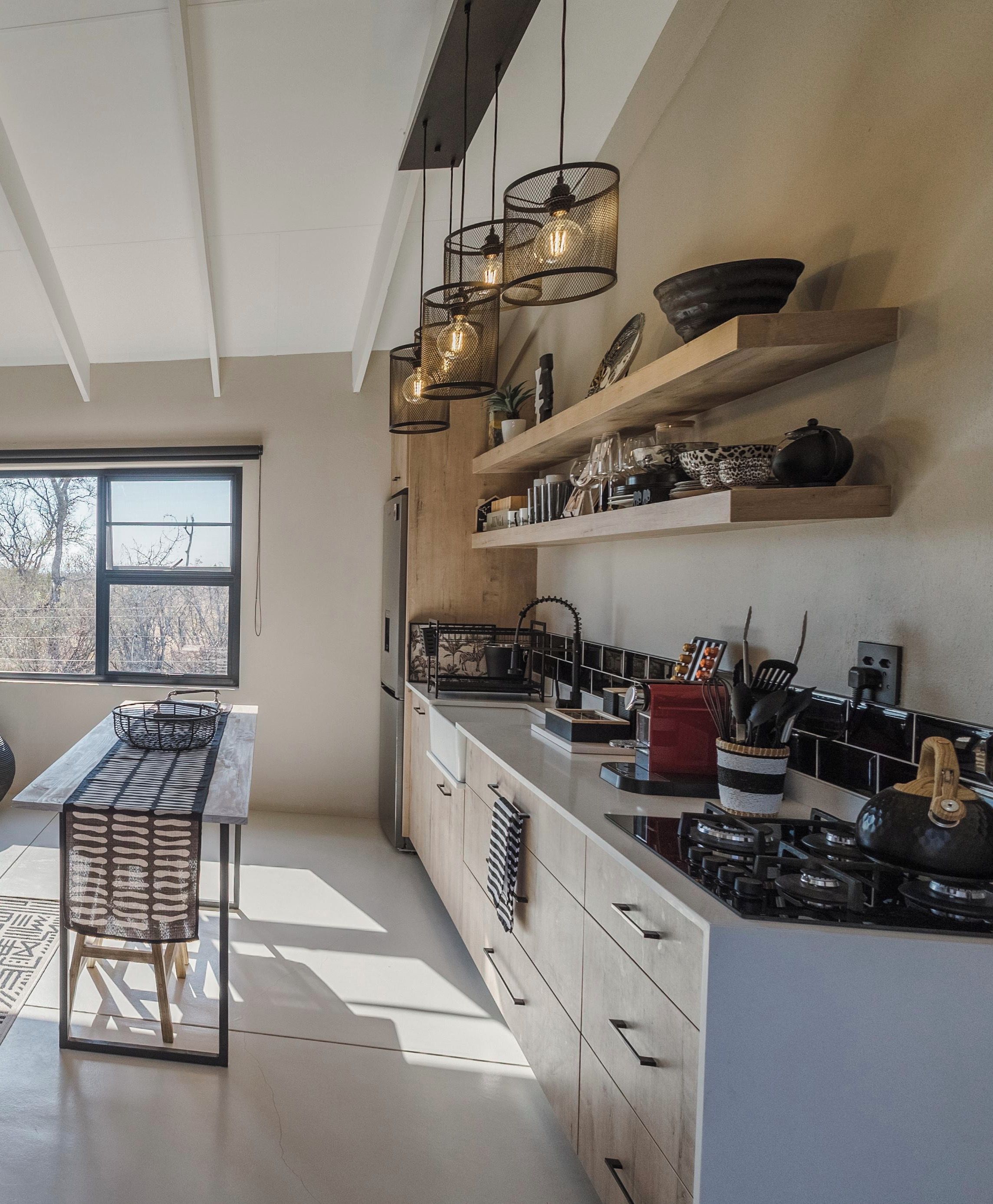 Une cuisine moderne dotée d’un îlot central, de luminaires suspendus et d’étagères intégrées.