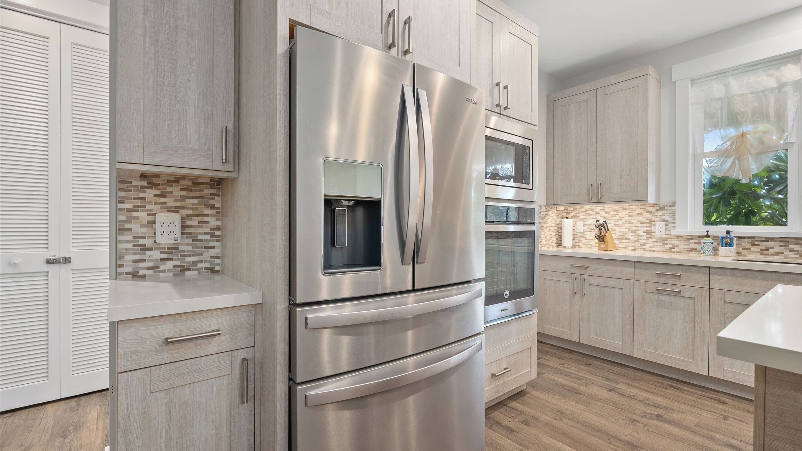 A modern kitchen with stainless steel appliances, a tiled backsplash, and light wood cabinetry.