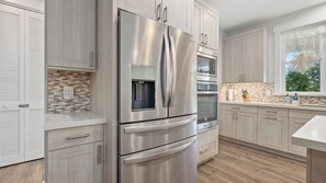 A modern kitchen with stainless steel appliances, a tiled backsplash, and light wood cabinetry. - Hale Pōmaikai by Avantstay Ocean View Lanai + Covered Dining Minutes to Poipu Beach & Koloa (Koloa)